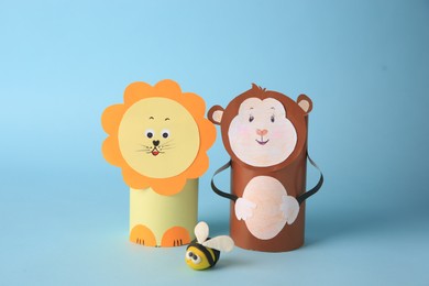 Photo of Toy monkey and lion made from toilet paper hubs with plasticine bee on light blue background. Children's handmade ideas