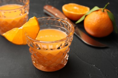 Photo of Tasty tangerine liqueur in glass and fresh citrus fruits on black textured table, closeup
