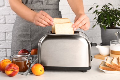 Photo of Woman putting bread into toaster in kitchen, closeup