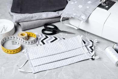 Photo of Sewing machine, homemade protective masks and craft accessories on grey marble table