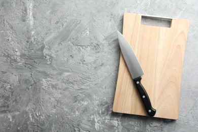 Photo of Knife and wooden board on grey textured table, top view. Space for text