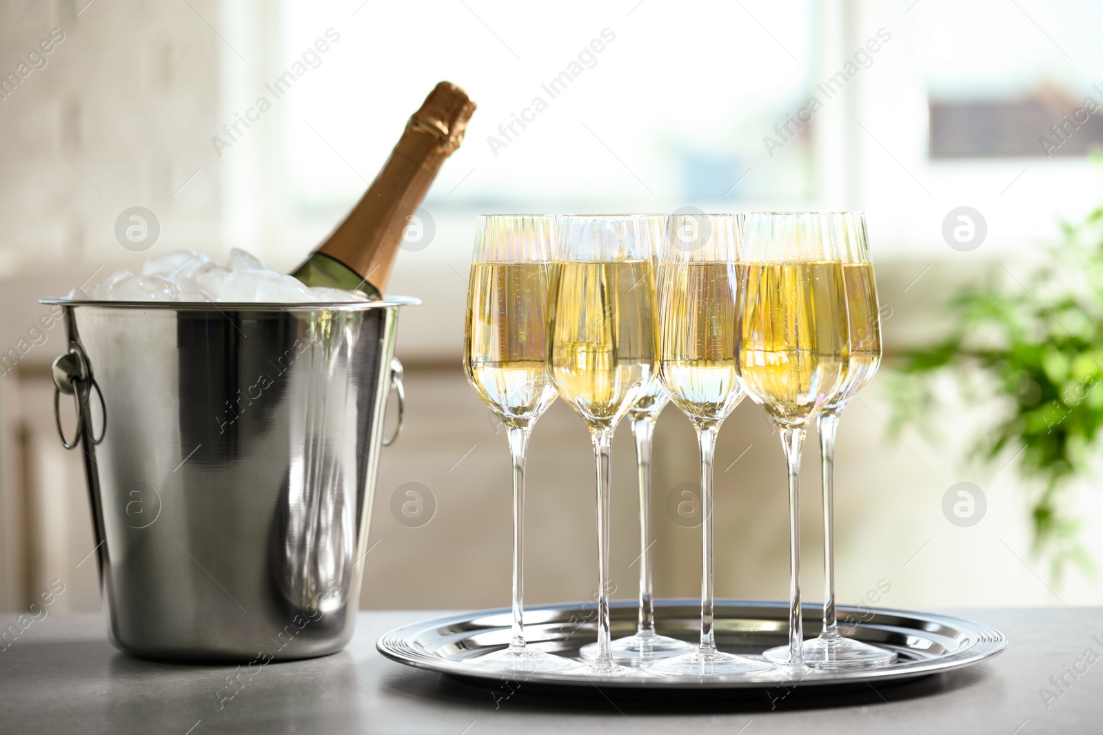 Photo of Glasses of champagne and ice bucket with bottle on grey table