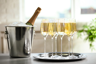 Glasses of champagne and ice bucket with bottle on grey table