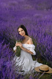 Beautiful young woman with bouquet sitting in lavender field