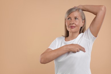 Photo of Beautiful senior woman doing breast self-examination on light brown background. Space for text