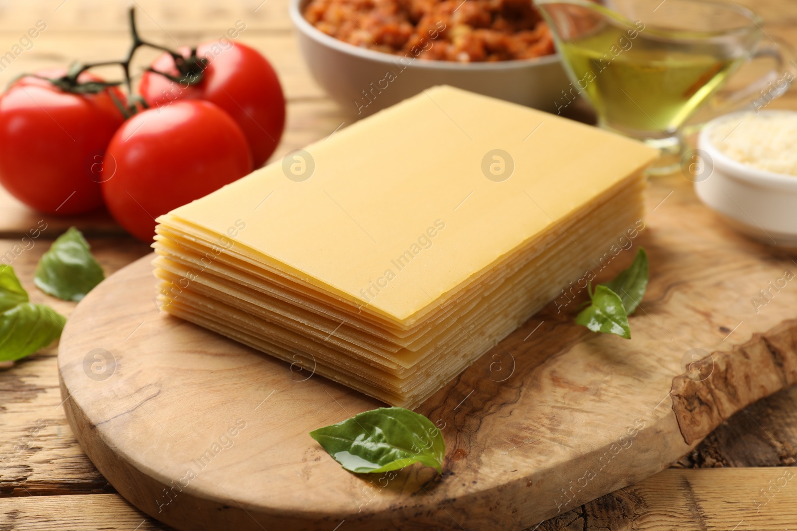 Photo of Cooking lasagna. Board with pasta sheets and other products on wooden table, closeup