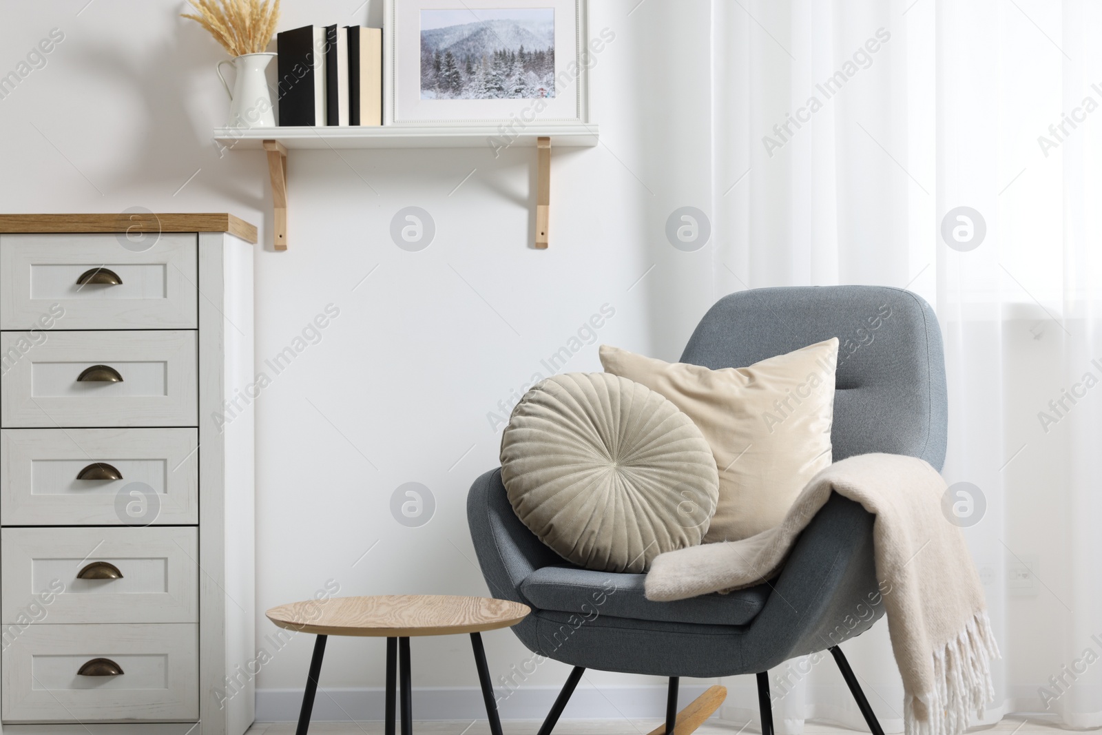 Photo of Soft pillows and blanket on rocking armchair indoors