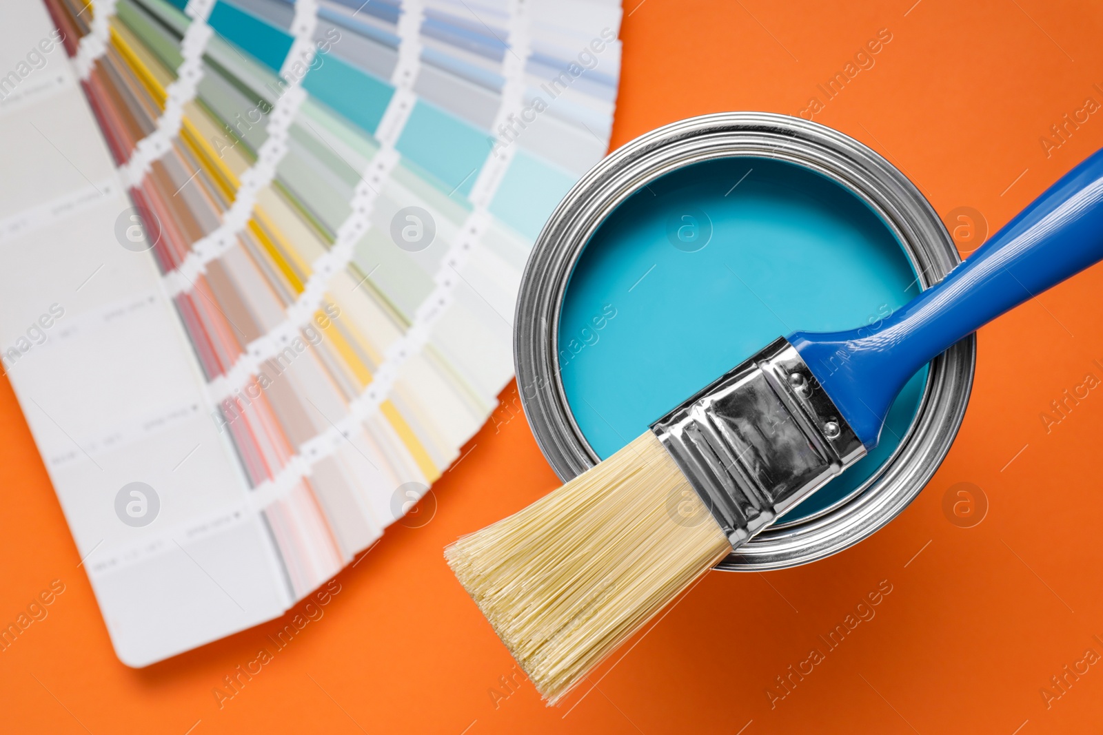 Photo of Can with light blue paint, brush and color palette on orange background, flat lay