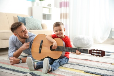 Photo of Father teaching his little son to play guitar at home