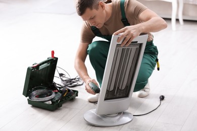 Photo of Professional technician repairing electric ultrared heater with screw gun indoors