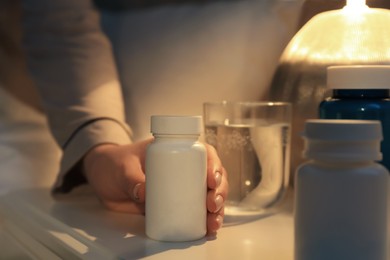 Woman taking pills from nightstand indoors, closeup. Insomnia treatment