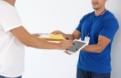 Young courier with envelopes and client signing on tablet against white background, closeup