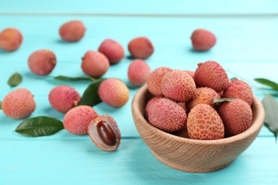 Photo of Fresh ripe lychee fruits in bowl on light blue wooden table. Space for text