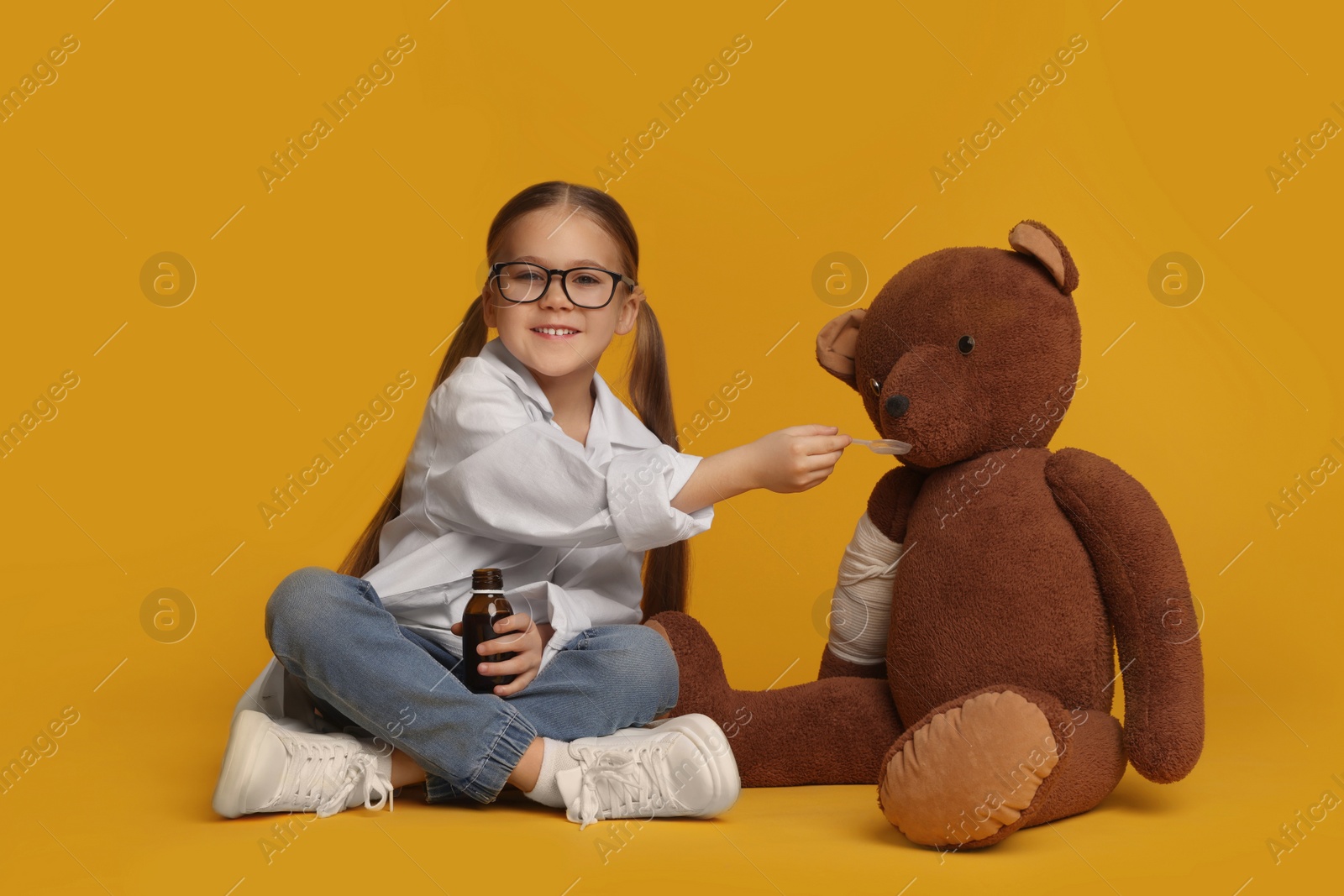 Photo of Little girl playing doctor with toy bear on yellow background