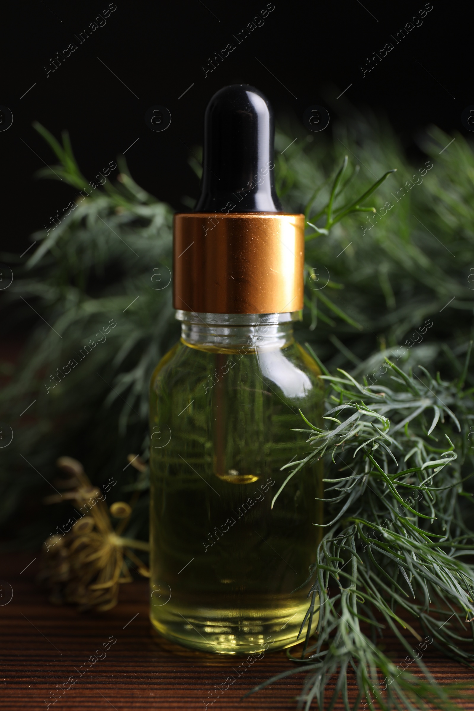 Photo of Bottle of essential oil and fresh dill on wooden table