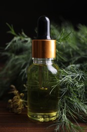 Photo of Bottle of essential oil and fresh dill on wooden table