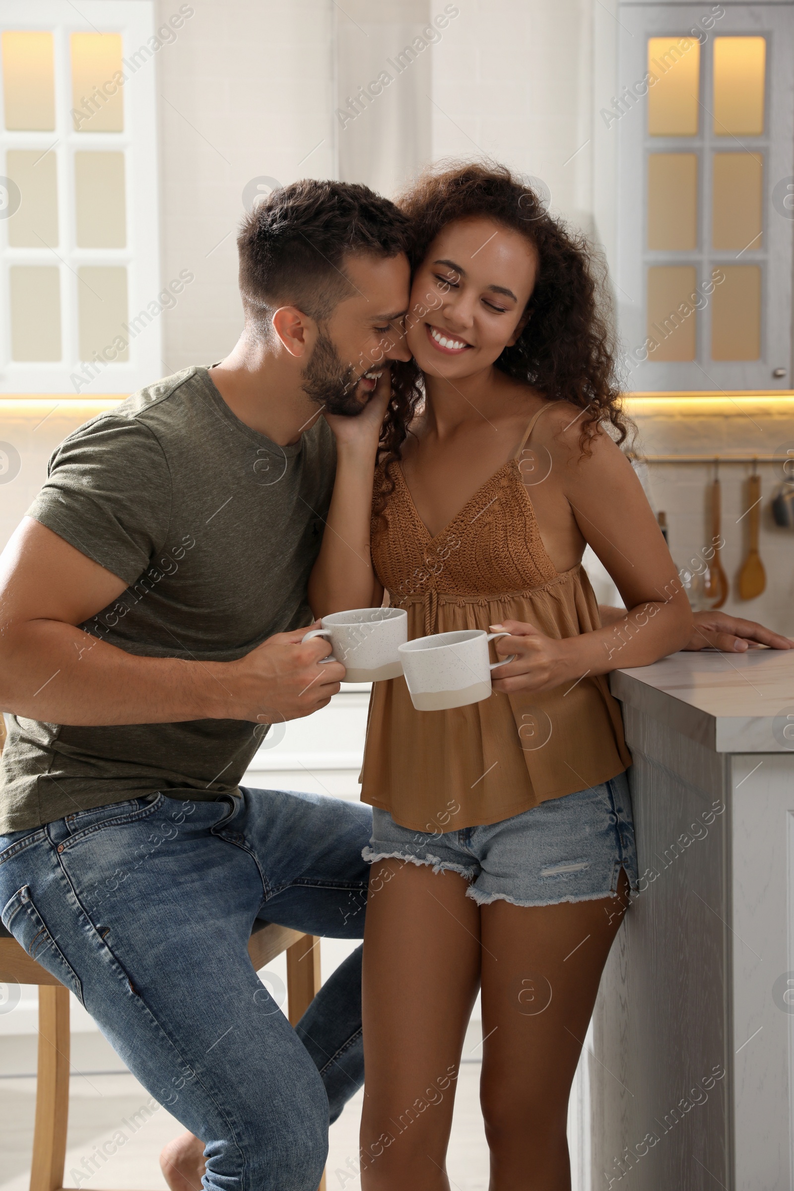 Photo of Lovely couple with cups of drink enjoying time together in kitchen at home