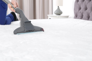 Photo of Man disinfecting mattress with vacuum cleaner, closeup. Space for text