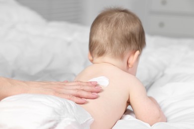 Photo of Woman applying body cream onto baby`s back on bed, closeup