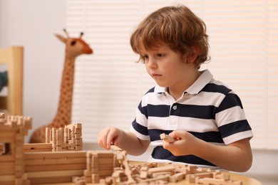 Photo of Cute little boy playing with wooden construction set at table in room. Child's toy