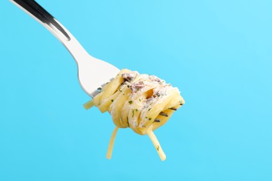 Photo of Fork with tasty pasta on light blue background, closeup