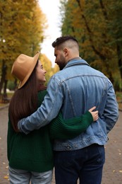 Photo of Happy young couple spending time together in autumn park, back view