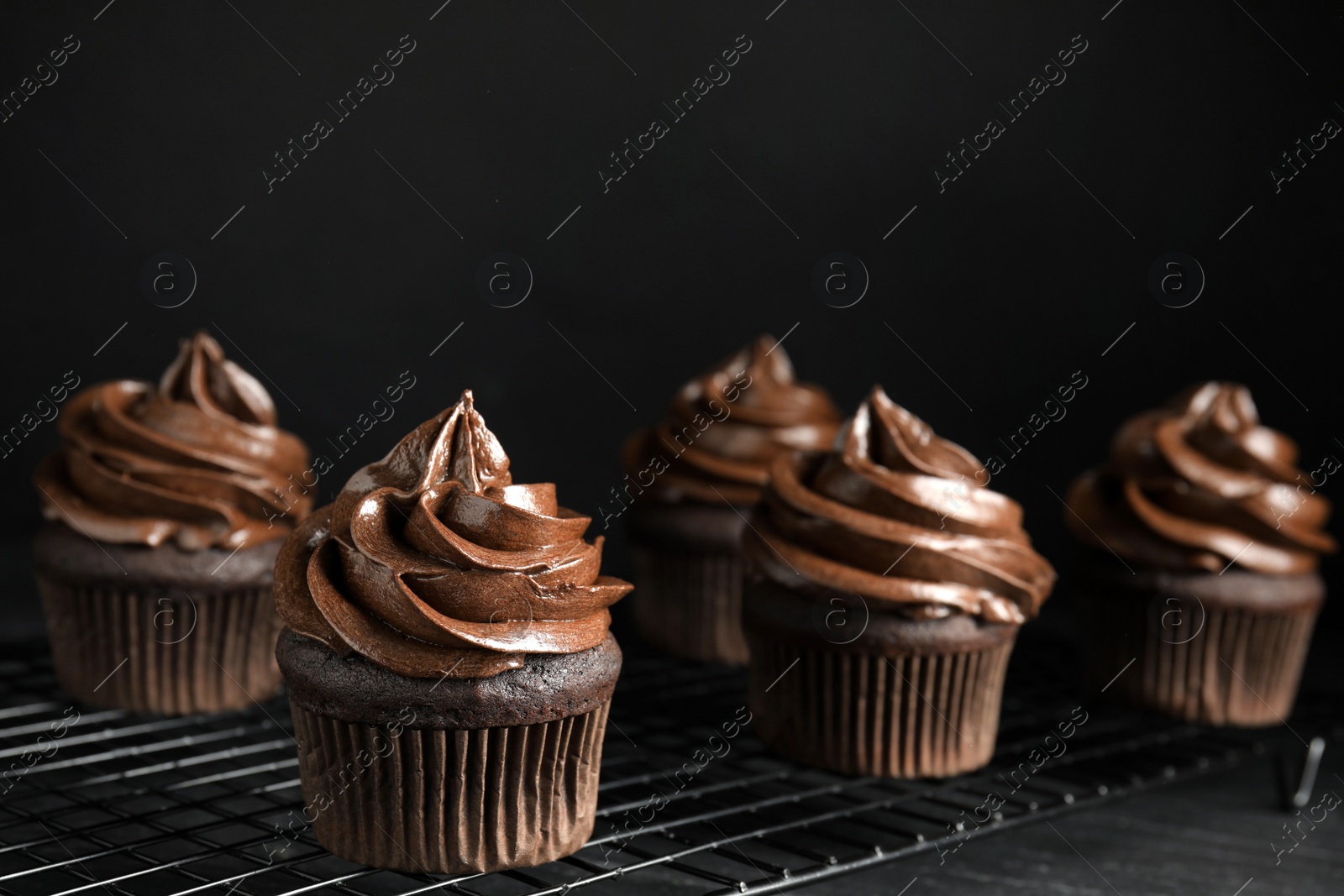 Photo of Cooling rack with delicious chocolate cupcakes on black table against dark background. Space for text