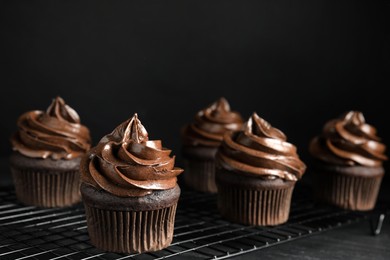 Cooling rack with delicious chocolate cupcakes on black table against dark background. Space for text