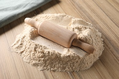 Photo of Pile of flour and rolling pin on wooden table, closeup