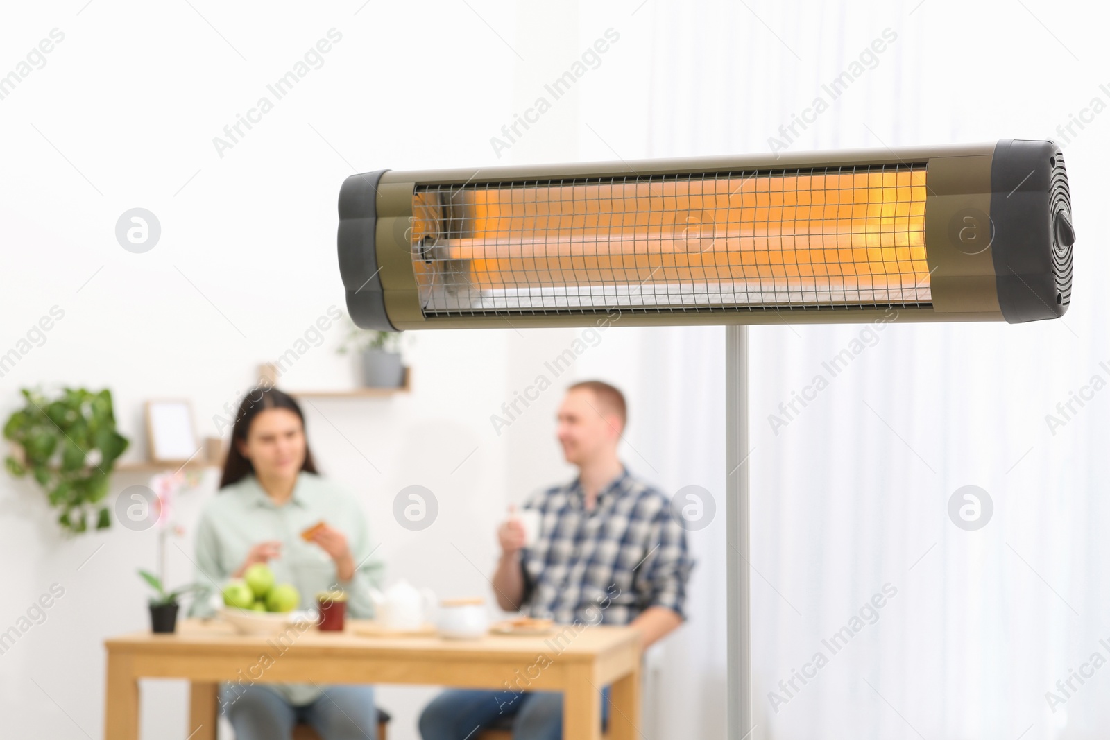 Photo of Couple spending time in room with modern electric infrared heater, focus on appliance