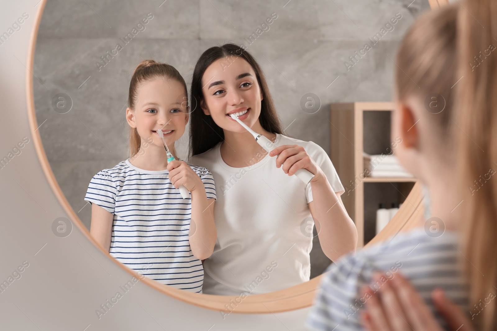 Photo of Mother and her daughter brushing teeth together near mirror in bathroom