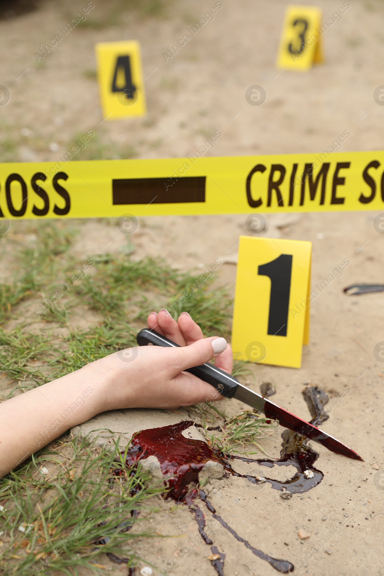 Photo of Crime scene with dead woman's body, bloody knife, markers and yellow tape outdoors, closeup