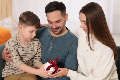 Photo of Happy family with gift on sofa at home