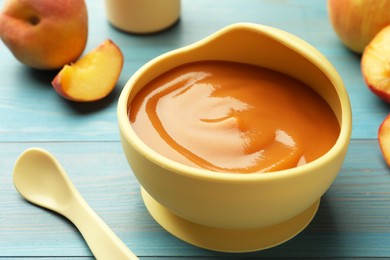 Bowl of tasty pureed baby food and ingredients on light blue wooden table, closeup