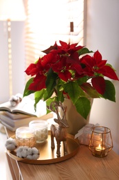 Photo of Beautiful poinsettia, burning candles and decorative deer on wooden table indoors. Traditional Christmas flower