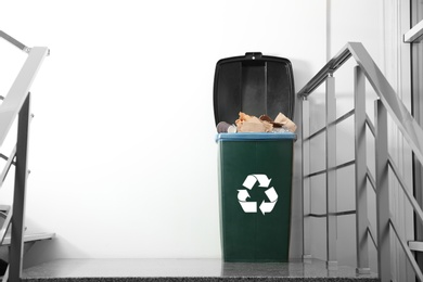 Full trash bin on stair landing indoors, space for text. Waste recycling