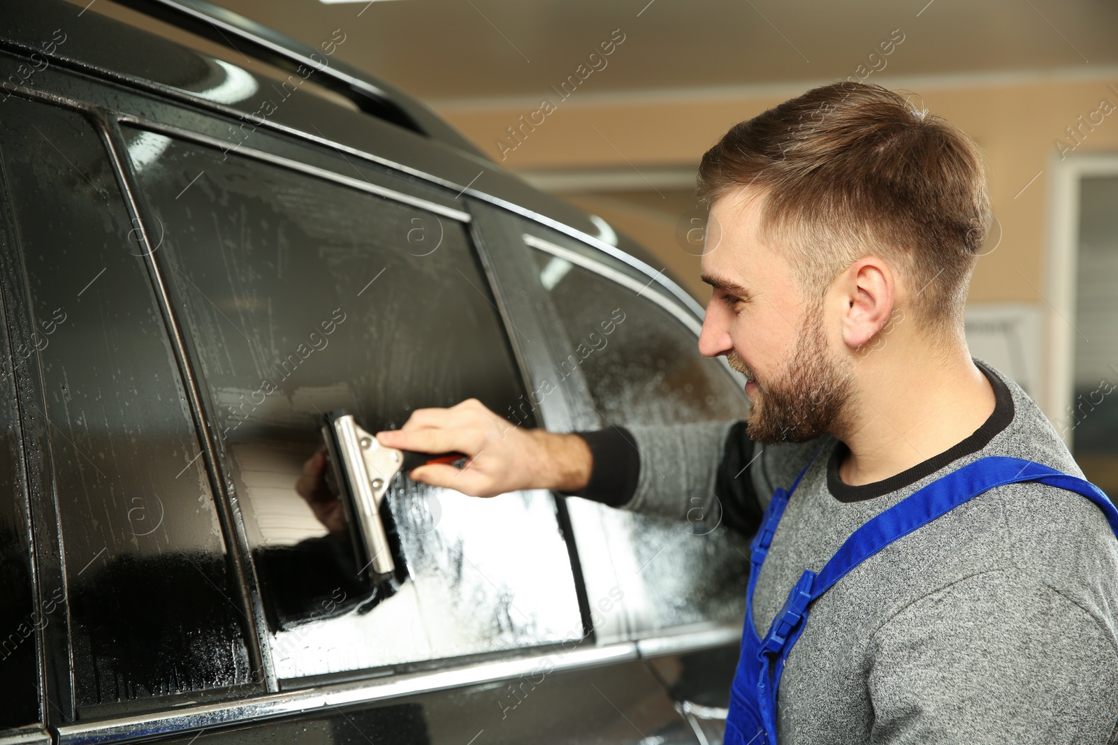 Photo of Skilled worker washing tinted car window in shop