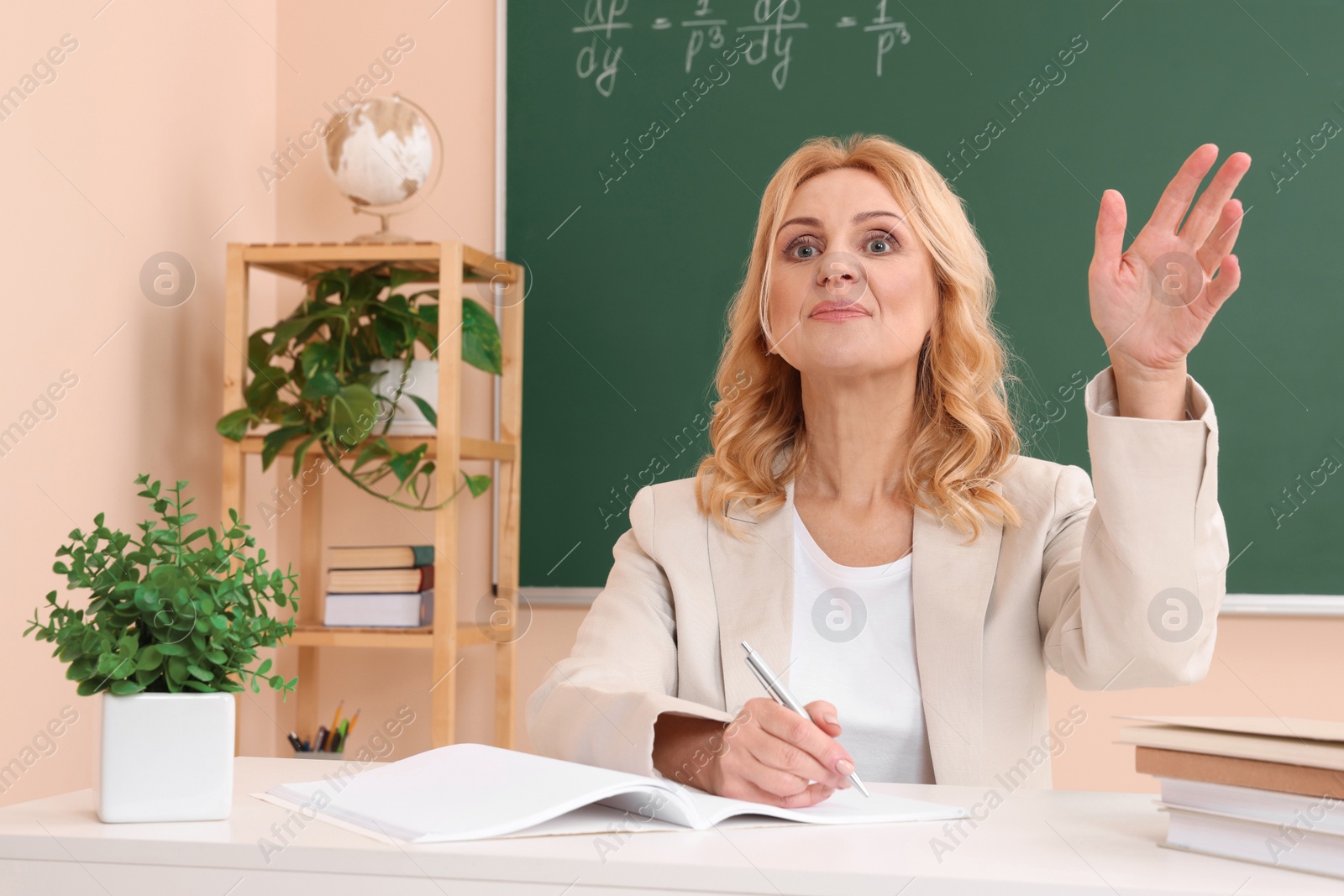 Photo of Professor giving lecture near green board at desk in classroom