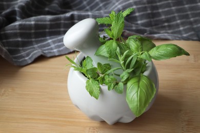 Photo of Mortar with different fresh herbs on wooden table, closeup