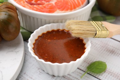 Photo of Fresh marinade, fish and brush on white wooden table, closeup