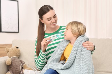 Mother helping her sick son with nebulizer inhalation at home