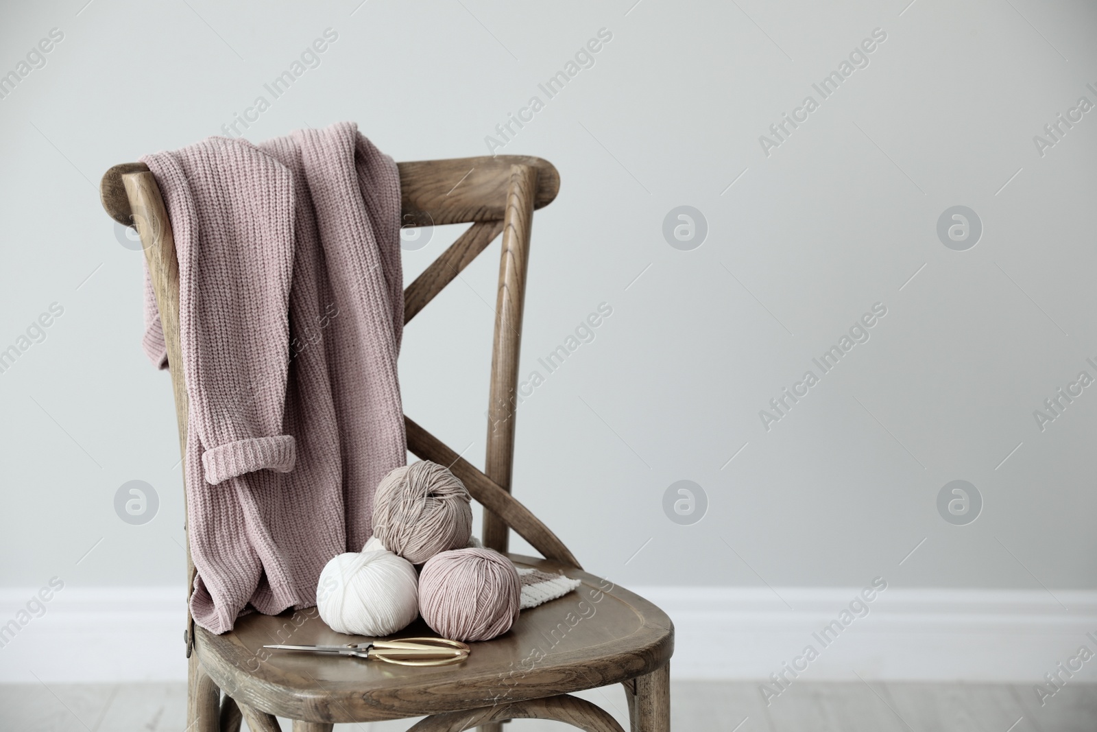 Photo of Yarn balls and scissors on wooden chair indoors, space for text. Creative hobby