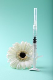 Photo of Cosmetology. Medical syringe and gerbera flower on turquoise background