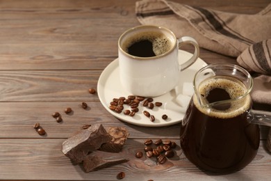 Glass turkish coffee pot, cup of hot drink, chocolate and beans on wooden table, space for text