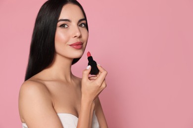Young woman with beautiful makeup holding glossy lipstick on pink background, space for text