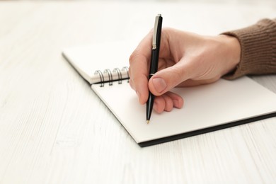Photo of Man writing in notebook at white wooden table, closeup. Space for text