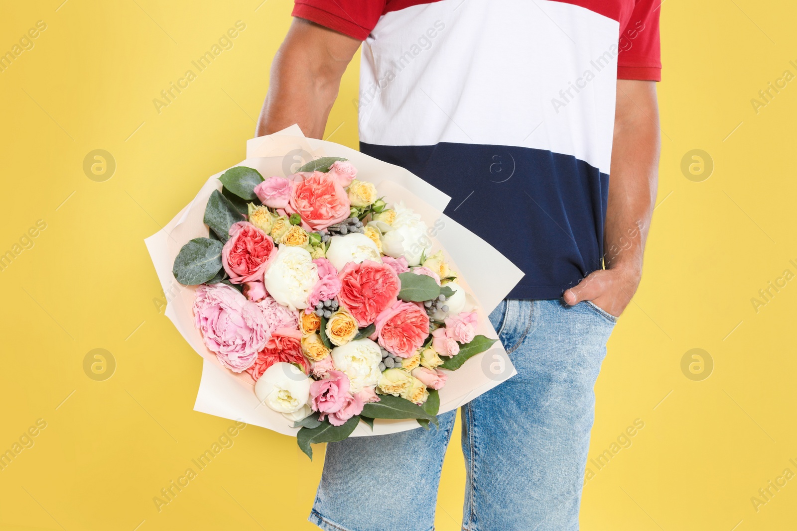 Photo of Young handsome man with beautiful flower bouquet on yellow background, closeup view