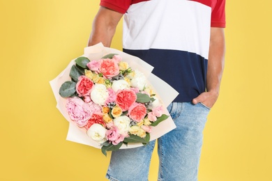 Young handsome man with beautiful flower bouquet on yellow background, closeup view