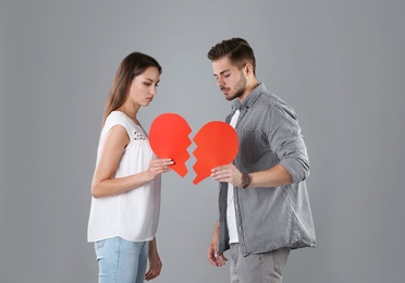 Photo of Young couple with torn paper heart on grey background. Relationship problems