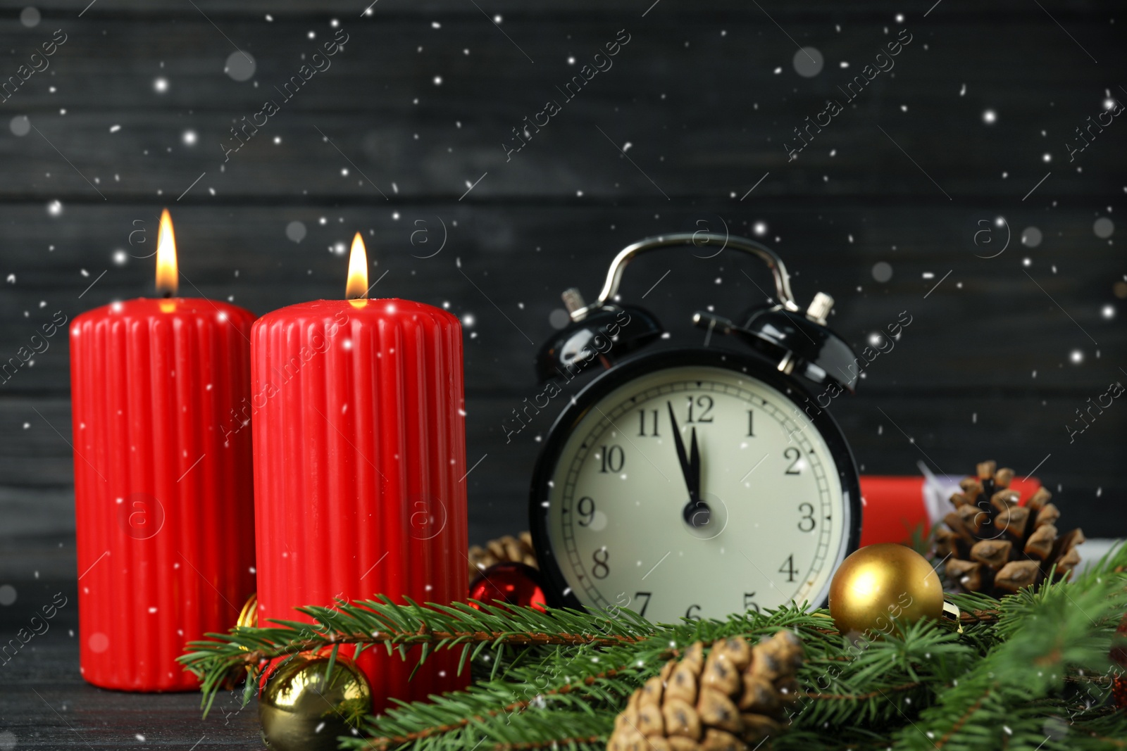 Photo of Snow falling on table with burning candles, alarm clock and festive decor. Christmas eve